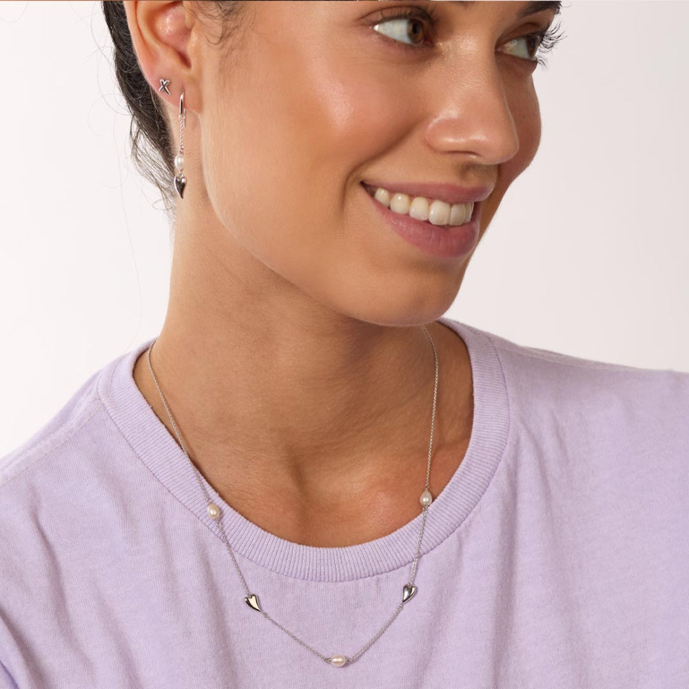 Woman wearing a delicate necklace with small heart pendants on a plain background