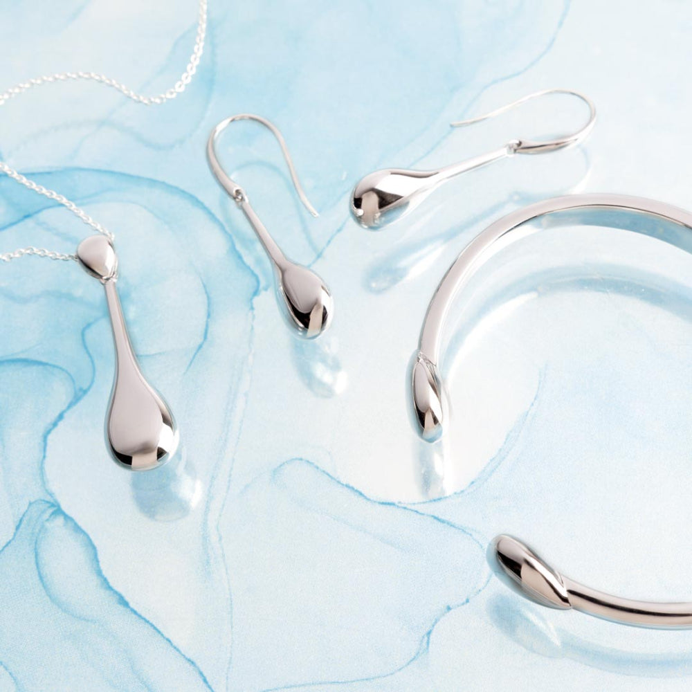 Silver jewelry set including necklace, earrings, and bracelet on a light blue marble background