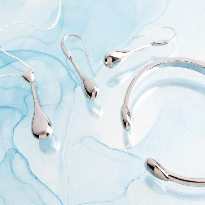 Silver jewelry set including necklace, earrings, and bracelet on a light blue marble background