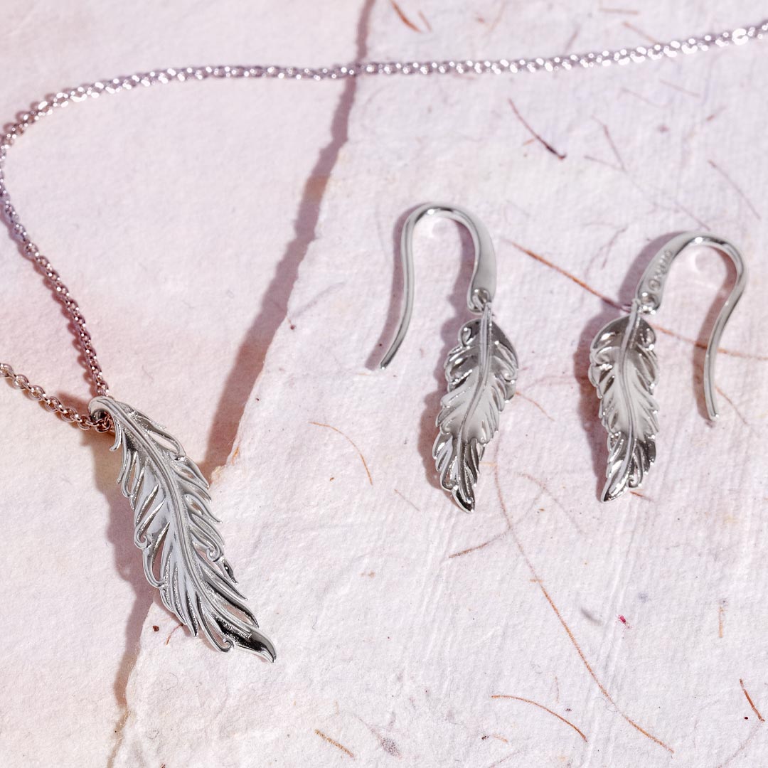 Silver feather necklace and earrings on a textured white surface