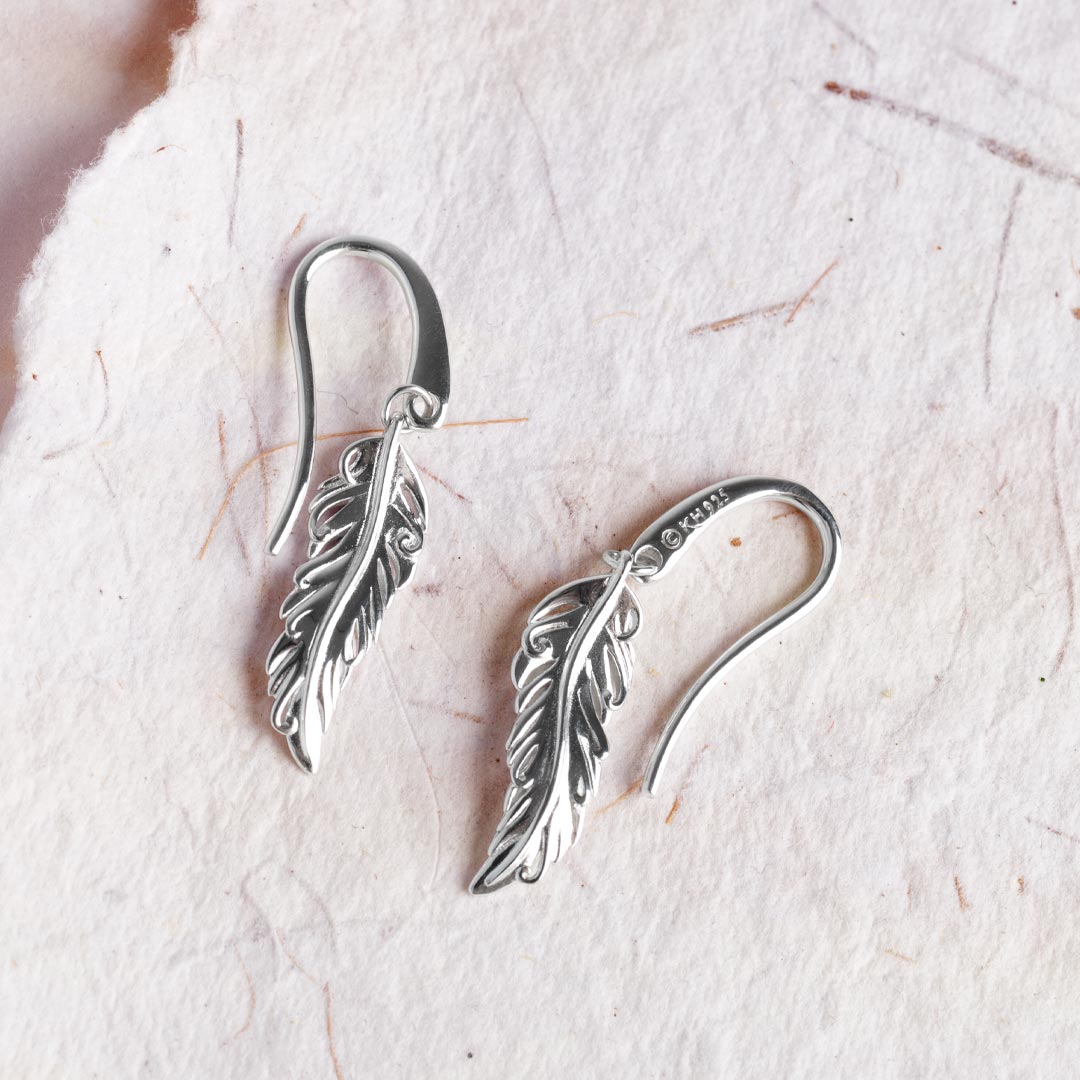Silver feather-shaped earrings on a light background