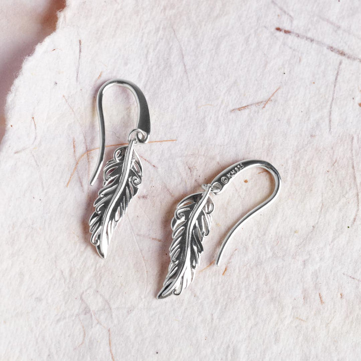 Silver feather-shaped earrings on a light background