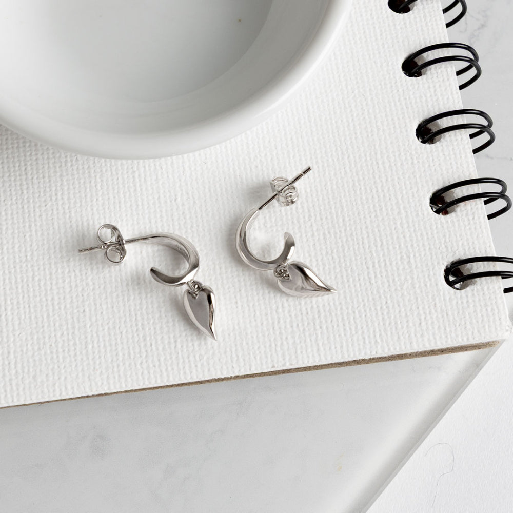 Silver earrings on a white surface with a notebook and pen in the background