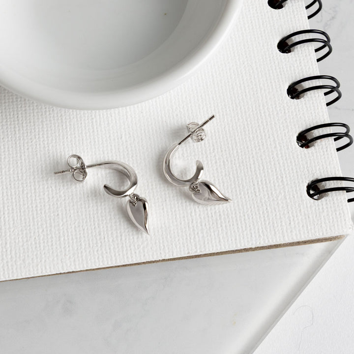 Silver earrings on a white surface with a notebook and pen in the background