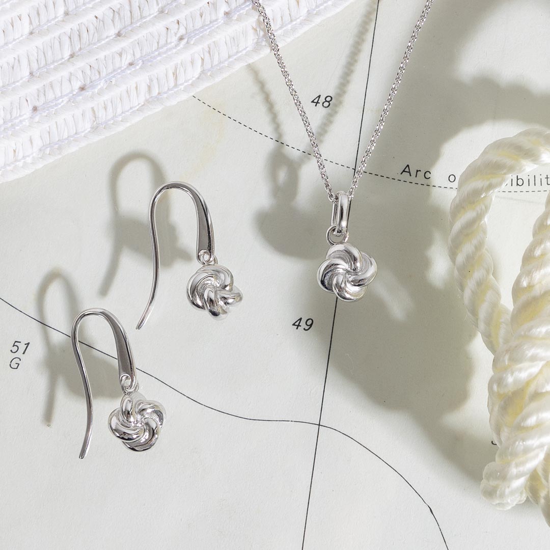 Silver knot pendant necklace and earrings on a light surface with a white flower.