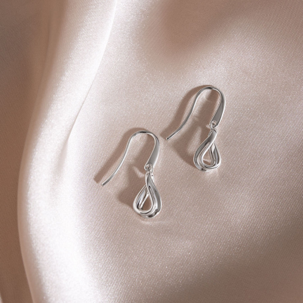 Pair of silver earrings on a soft pink fabric background