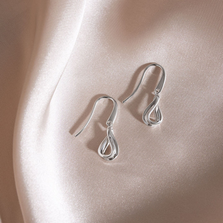 Pair of silver earrings on a soft pink fabric background