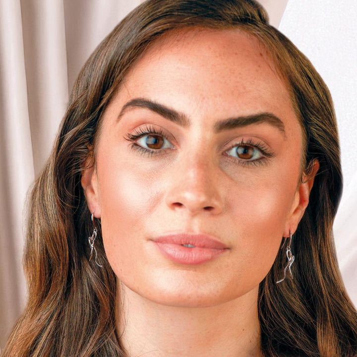 Close-up of a woman with long brown hair and earrings against a neutral background