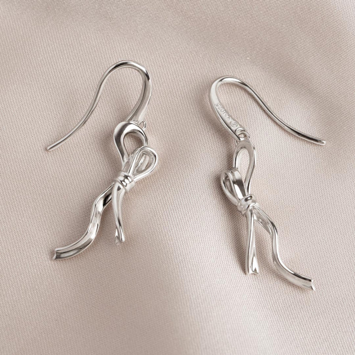 Silver bow-shaped earrings on a beige fabric background