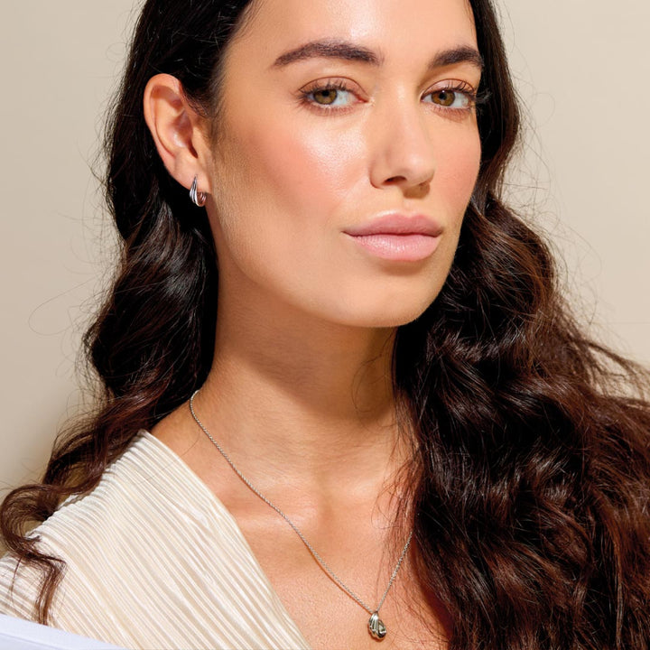 Close-up of a woman with long dark hair wearing a necklace against a neutral background