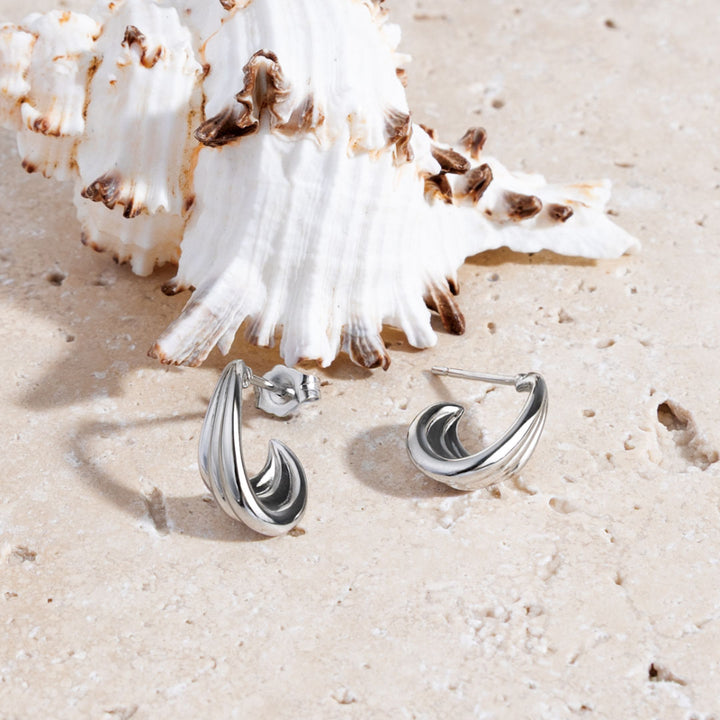 Silver earrings on a sandy surface with shells in the background