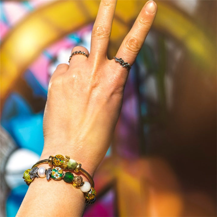 Hand with colorful beaded bracelet and ring, peace sign gesture against a blurred background