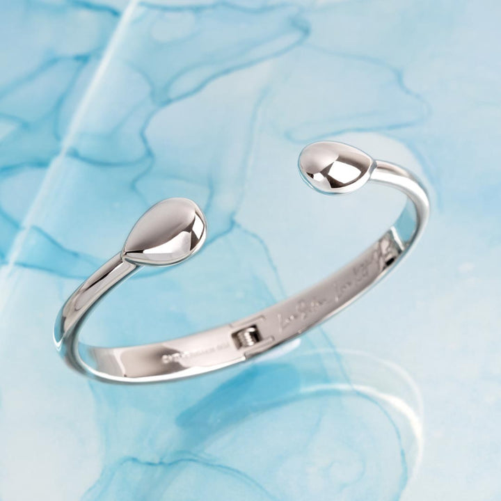 Silver bracelet with teardrop-shaped ends on a light blue textured background