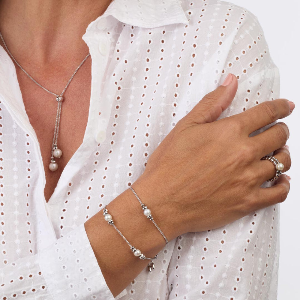 Person wearing a pearl bracelet and necklace with a white blouse.