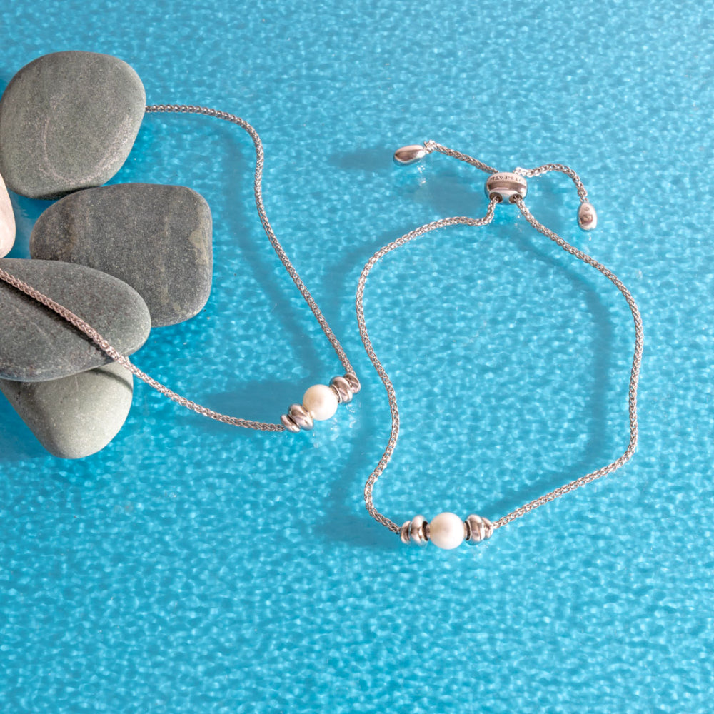 Silver bracelet with pearls on a blue textured surface with stones.