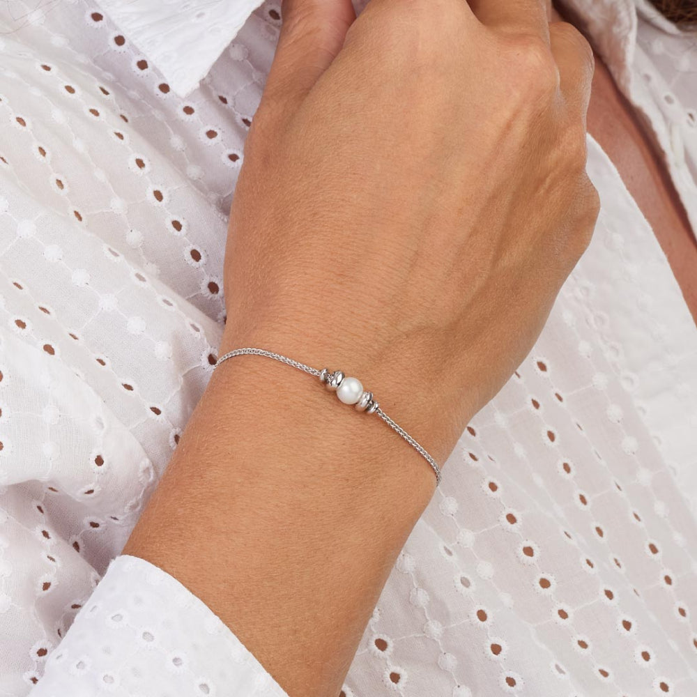 Hand wearing a silver bracelet with pearls against a white background