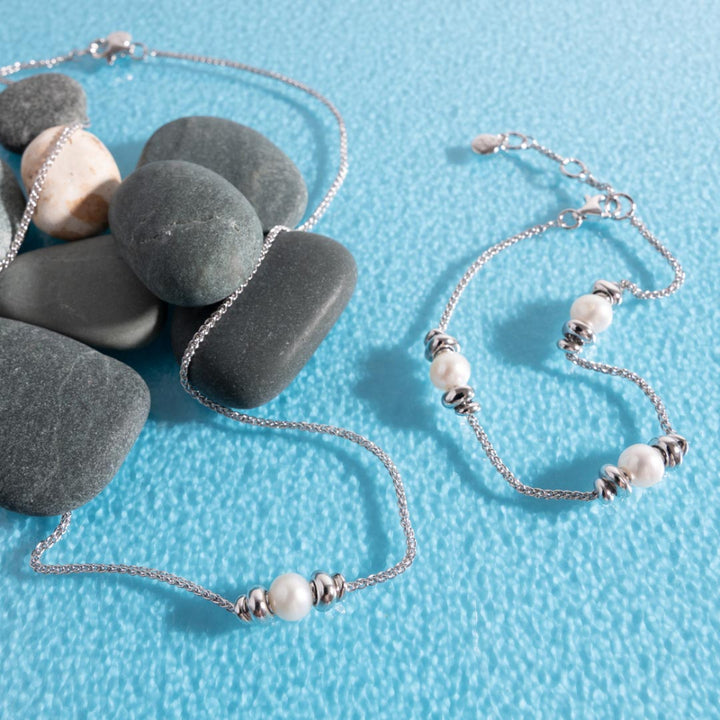 Silver necklace and bracelet with pearls on a blue textured background