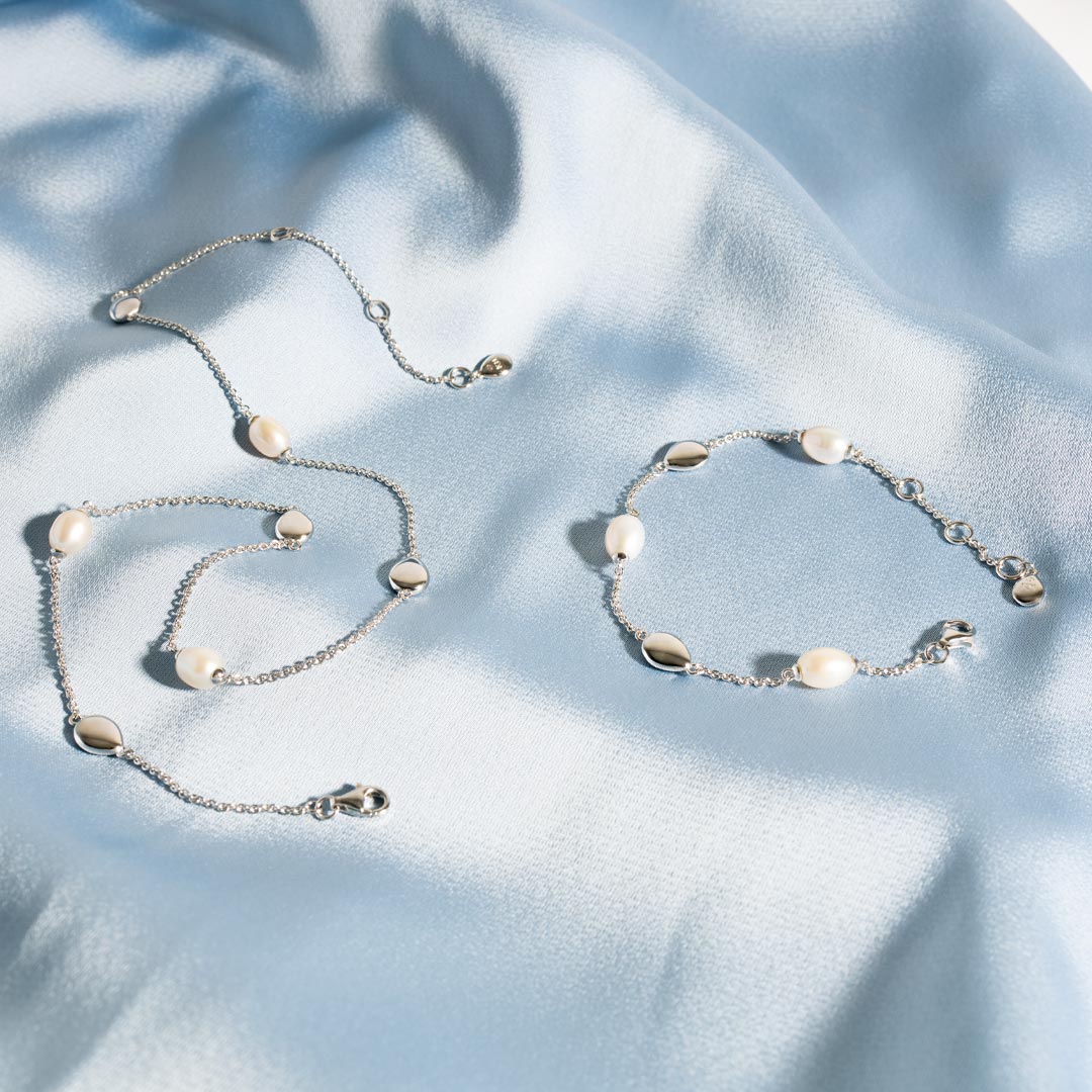 Silver jewelry set with pearls on a light blue fabric background