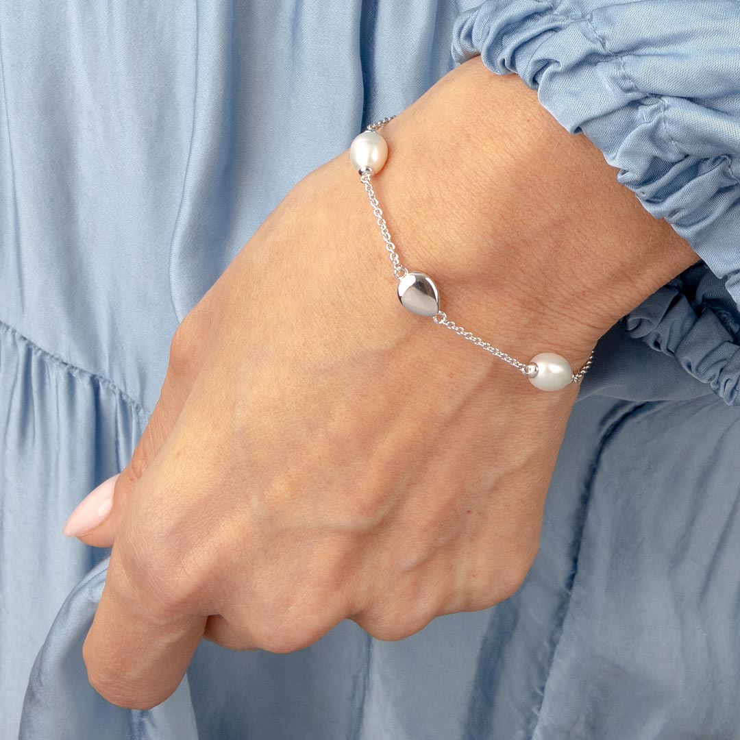 Silver bracelet with pearls on a wrist against a light blue fabric background