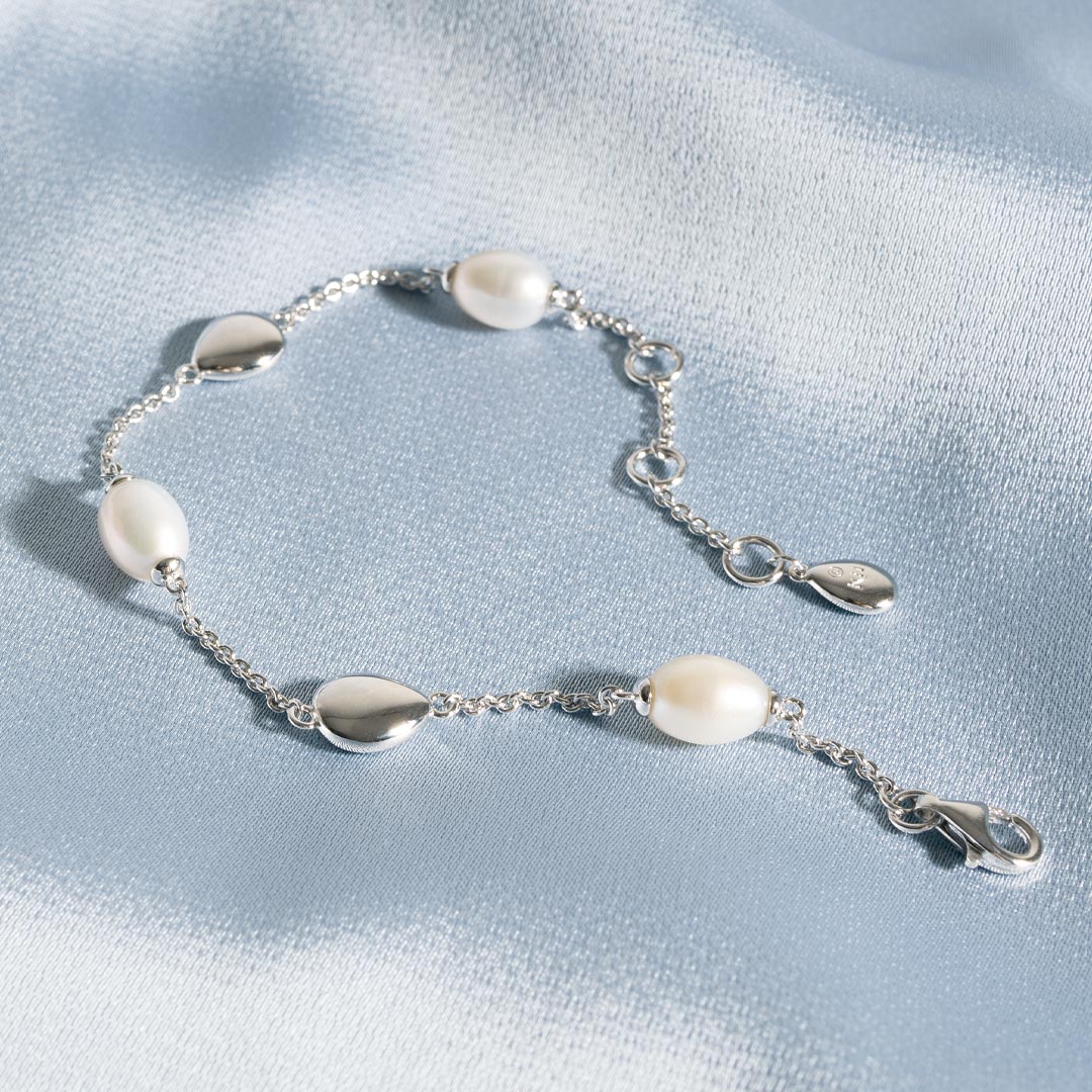 Silver bracelet with pearl beads on a light blue fabric background