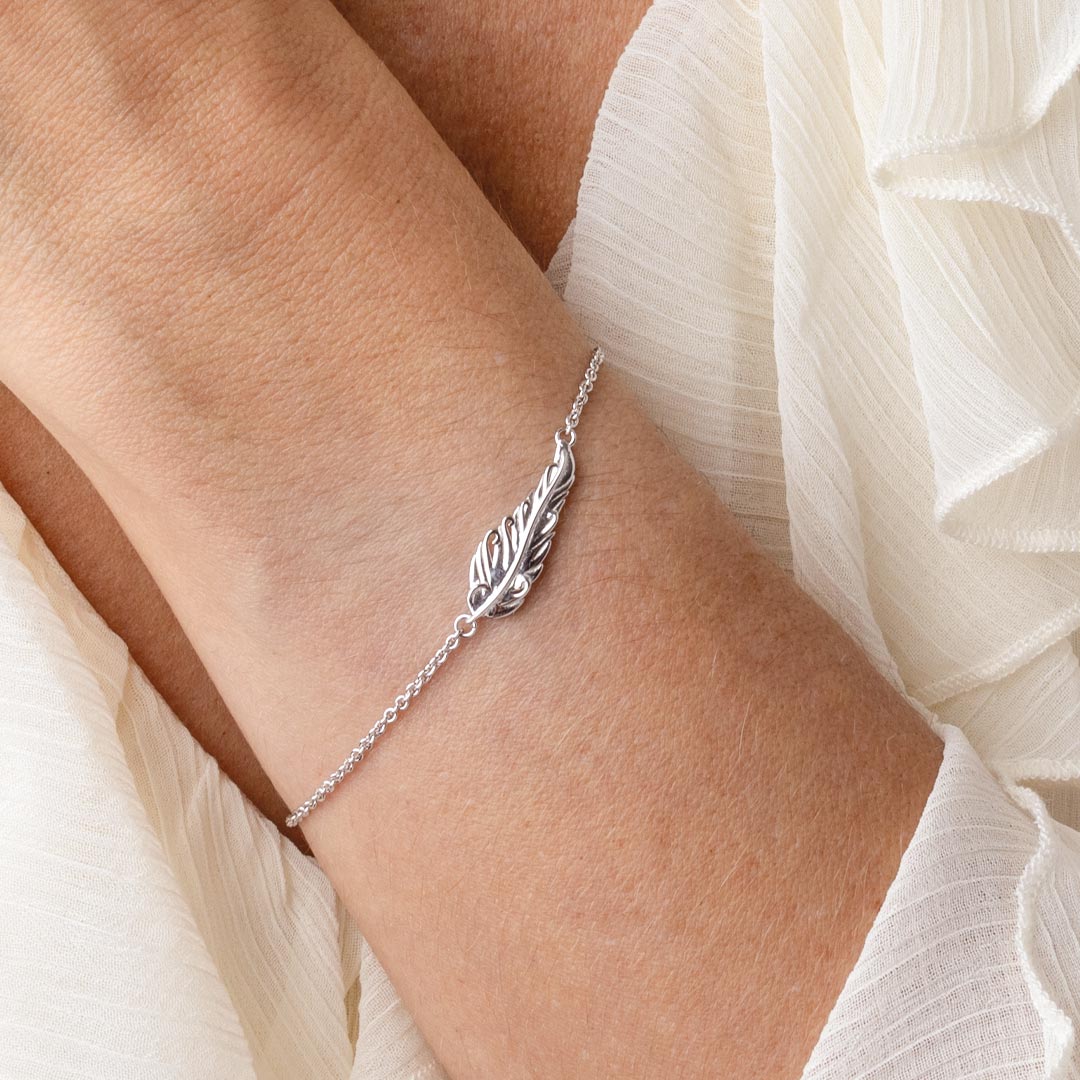 Silver feather bracelet on a wrist with a white fabric background
