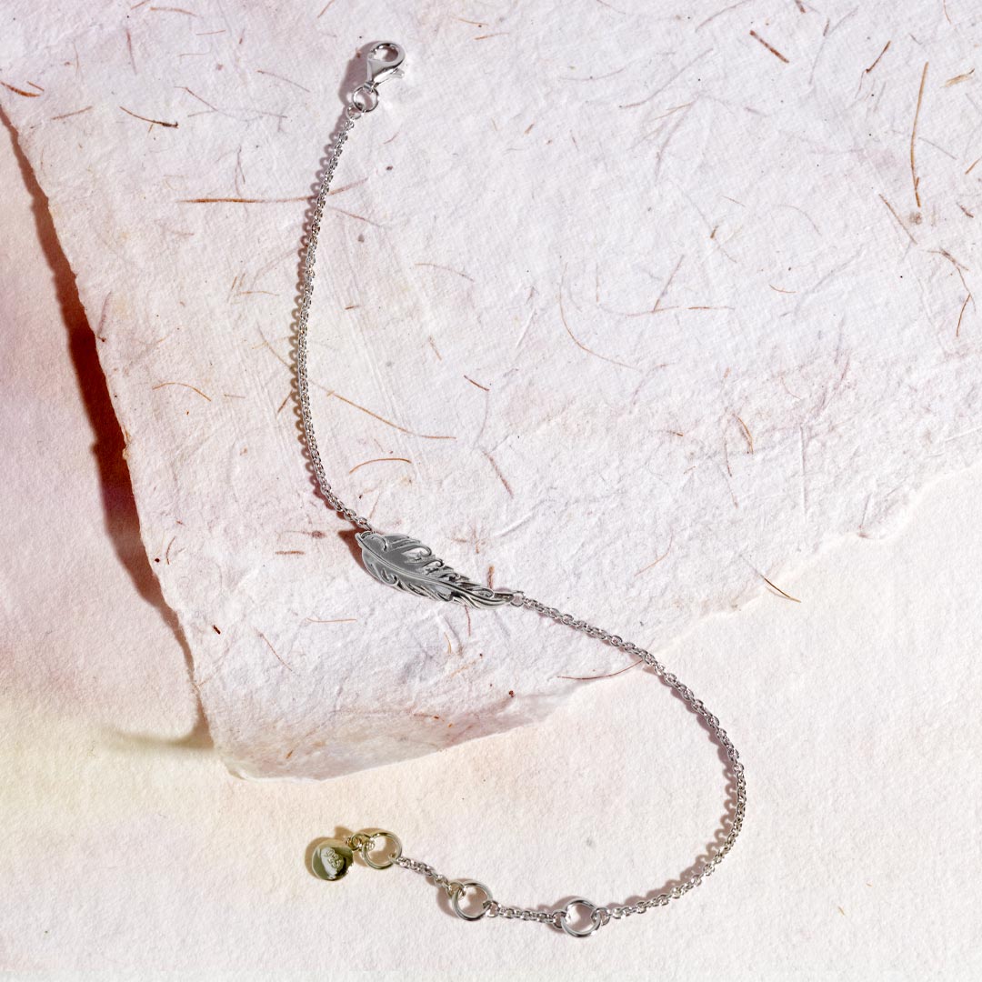 Silver bracelet with a leaf charm on a textured white surface