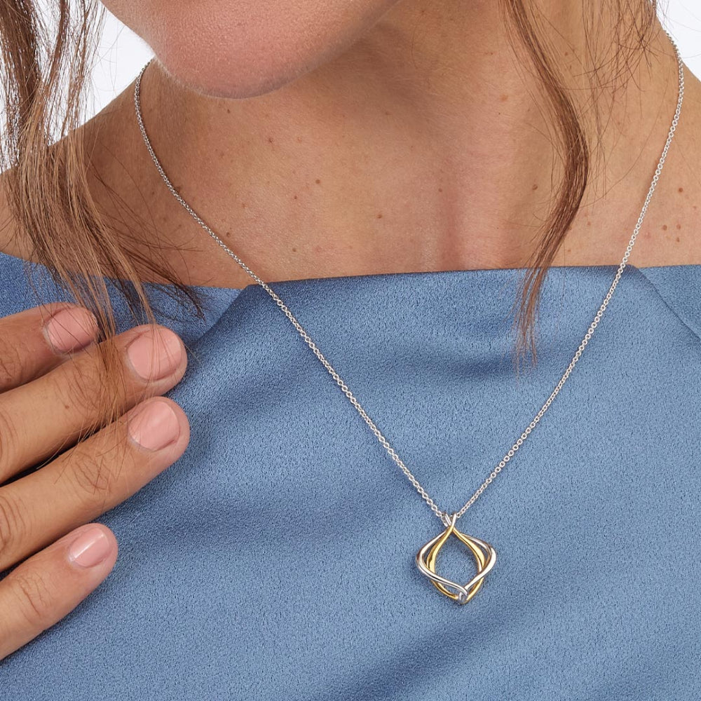 Necklace with a gold and silver pendant worn by a person on a blue background
