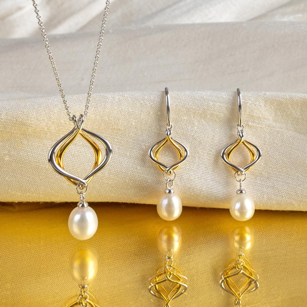 Jewelry set with a necklace and earrings featuring pearl drops on a yellow fabric background.