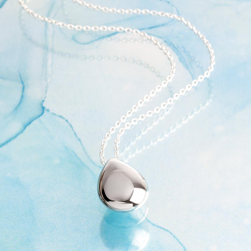 Silver necklace with a heart-shaped pendant on a light blue fabric background