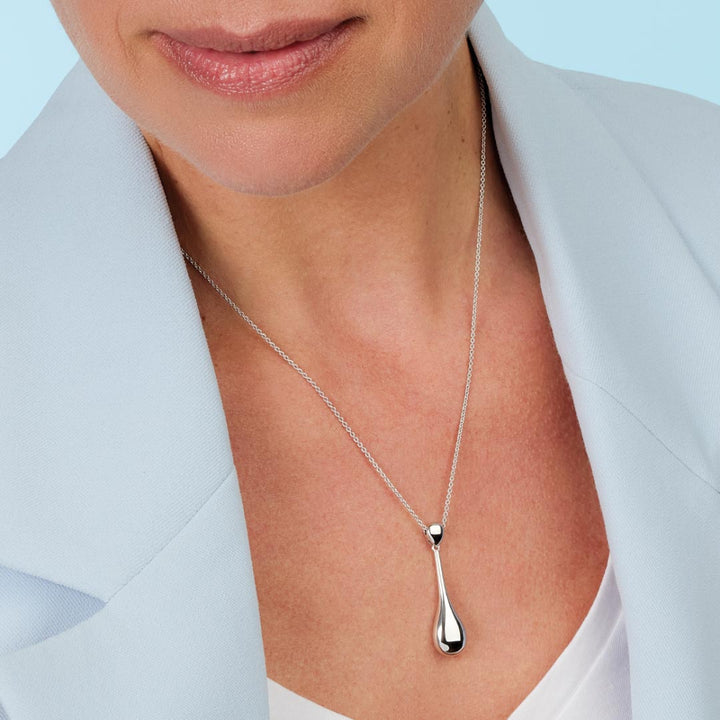 Silver teardrop pendant necklace on a person wearing a light blue blazer.