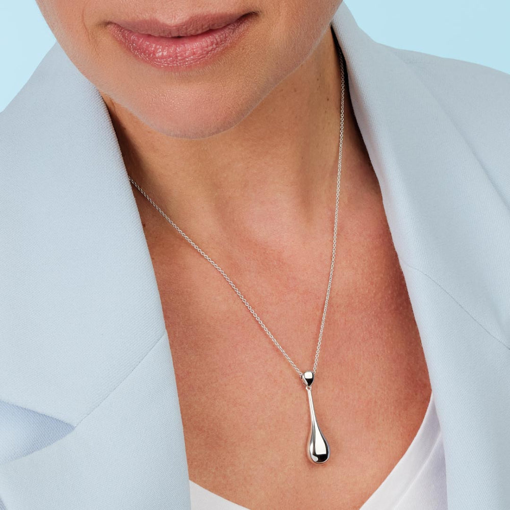 Silver teardrop pendant necklace on a person wearing a light blue blazer.