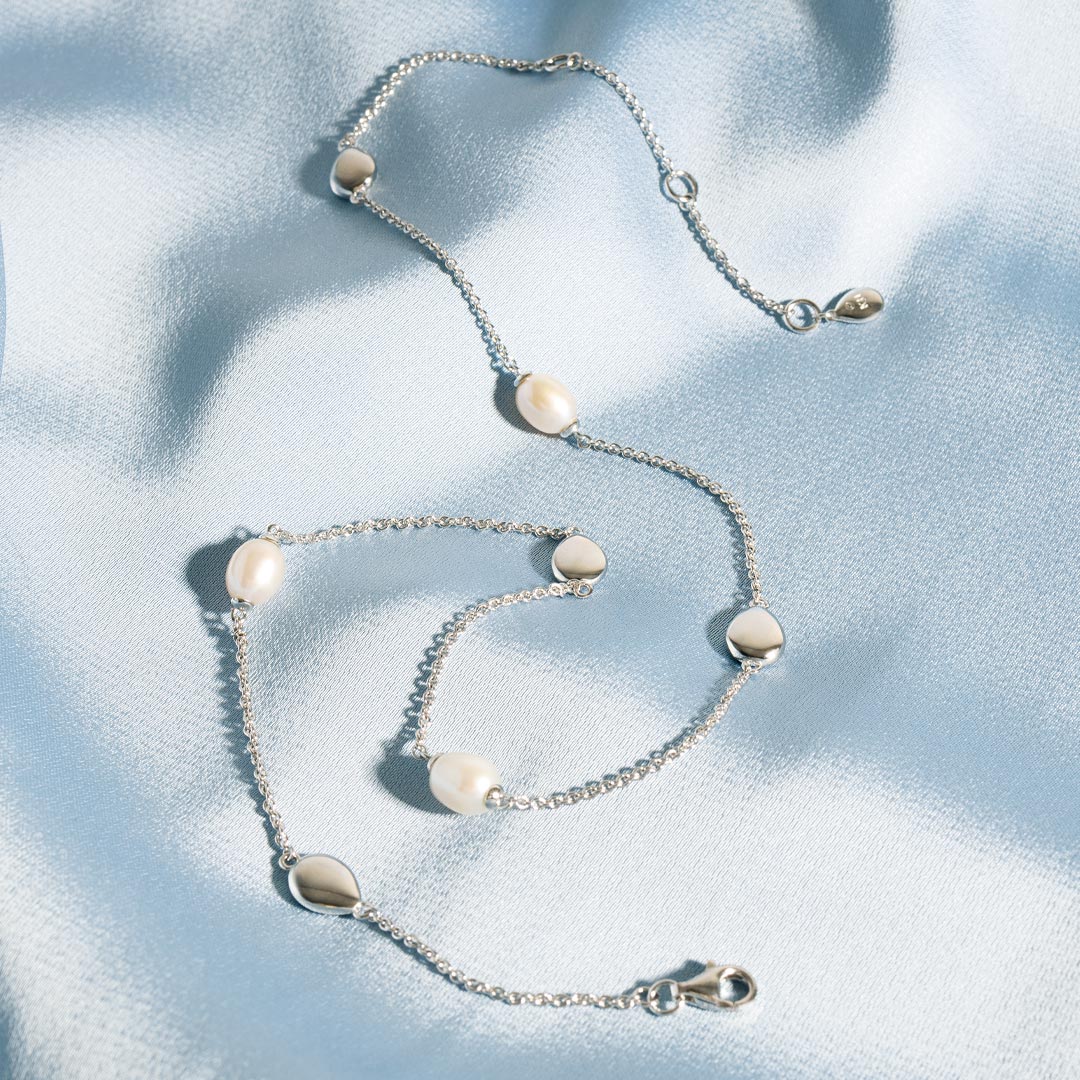 Silver necklace with pearl-like beads on a light blue fabric background
