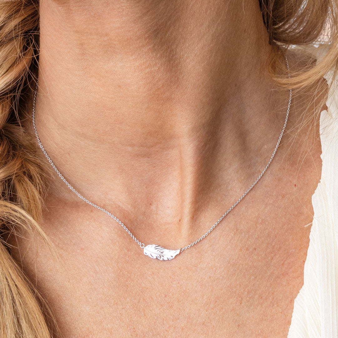 Silver necklace with a feather pendant on a person's neck
