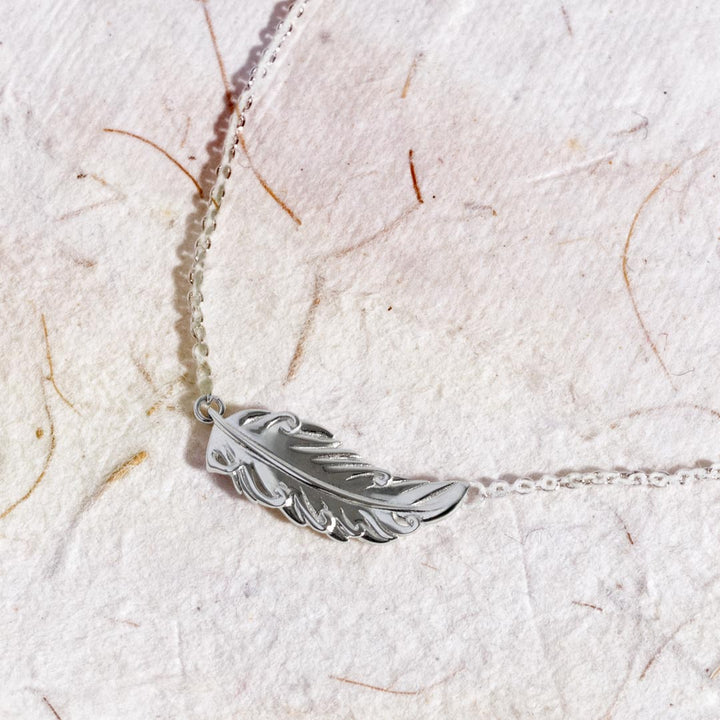 Silver feather necklace on a light textured fabric background