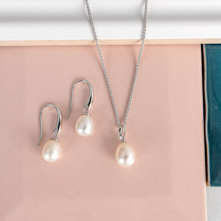 Pearl necklace and earrings set on a pink surface