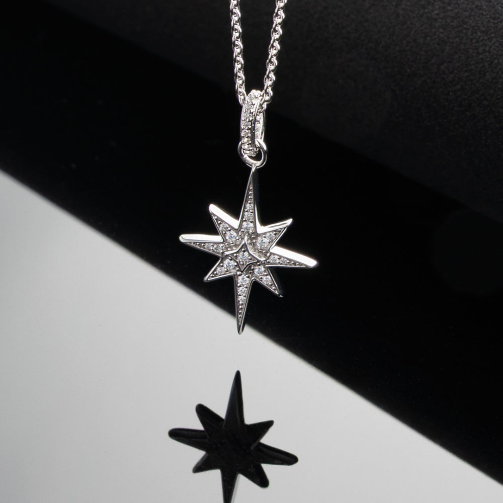 Star-shaped silver pendant on a chain against a black and white background