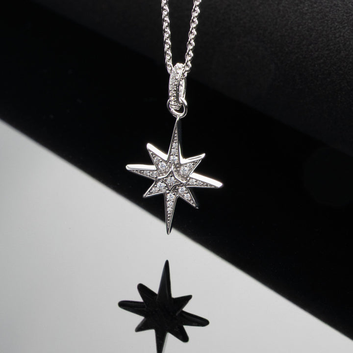 Star-shaped silver pendant on a chain against a black and white background