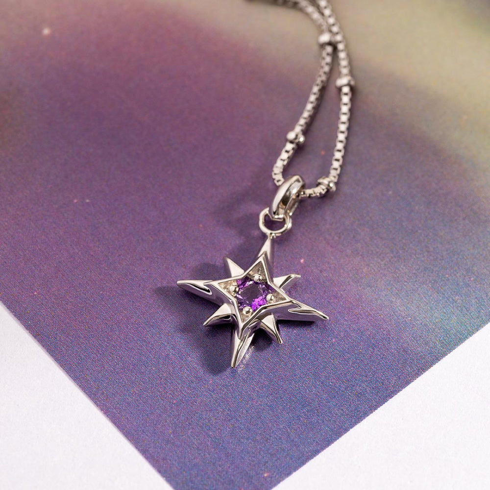 Silver star-shaped pendant with a purple gemstone on a reflective surface