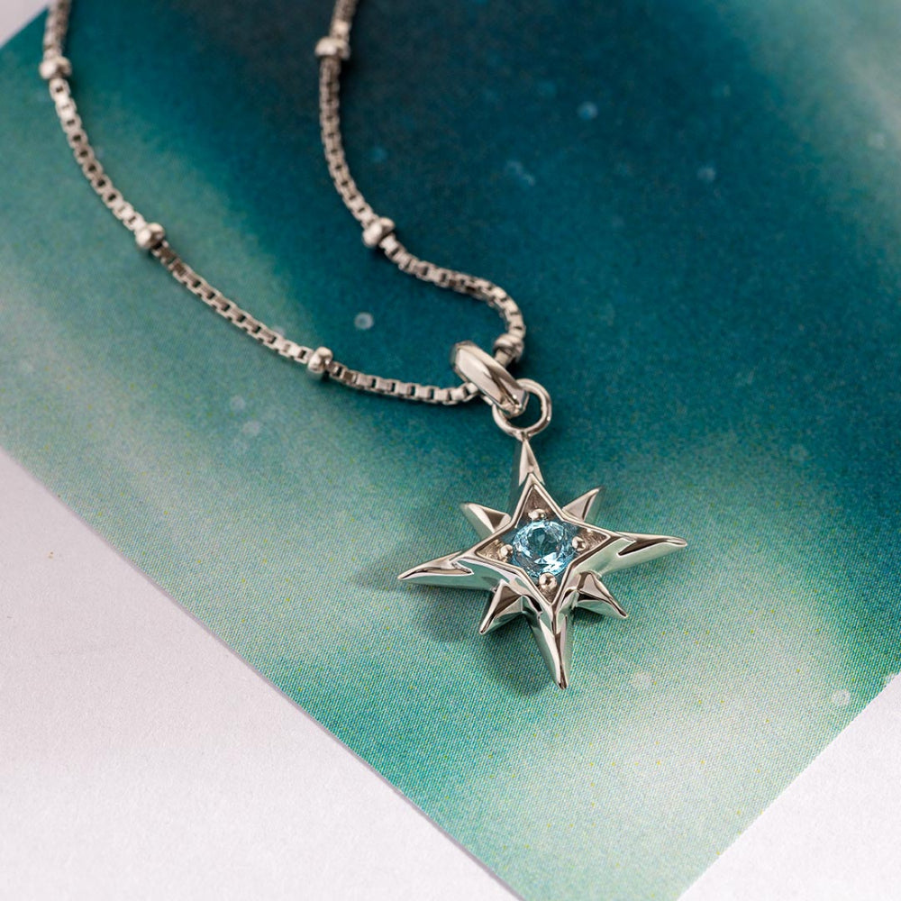 Silver star-shaped pendant with a blue gemstone on a chain against a teal background