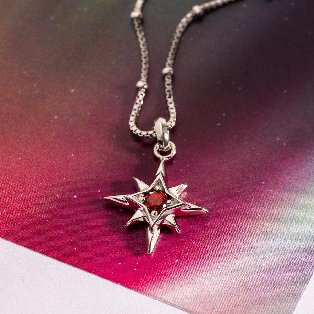 Silver star-shaped pendant with a red gemstone on a chain against a colorful gradient background