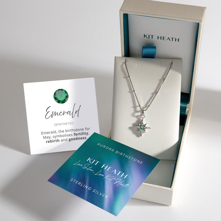 Silver necklace with star pendant and emerald stone in a Kit Heath box, accompanied by information cards.