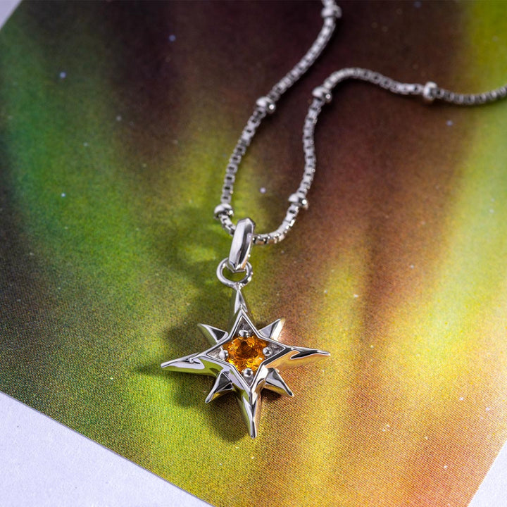 Silver star-shaped pendant with a yellow gemstone on a colorful background
