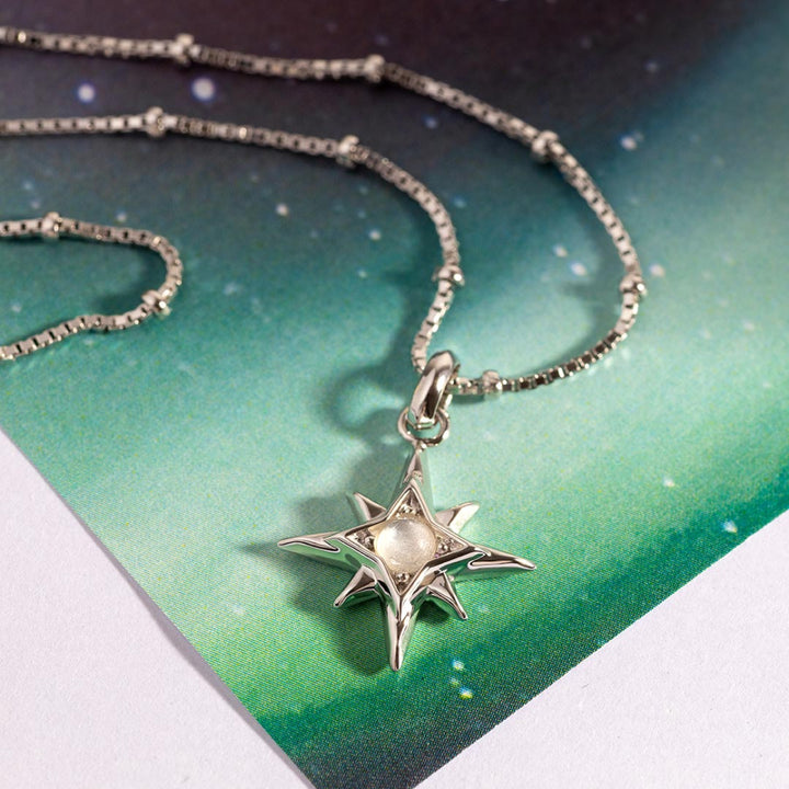 Silver star-shaped pendant necklace on a green and white background
