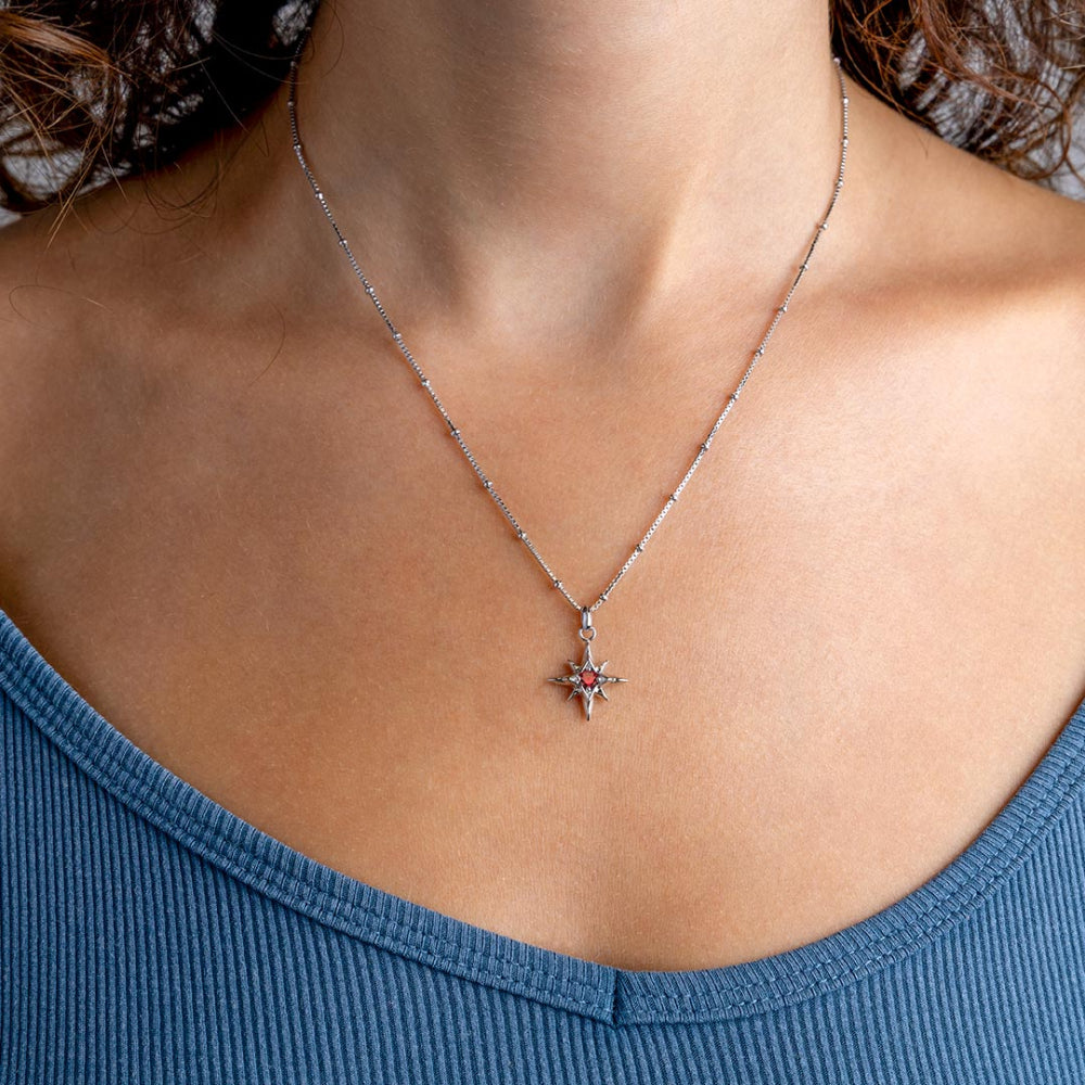 Silver necklace with a star-shaped pendant featuring a red gemstone on a white background