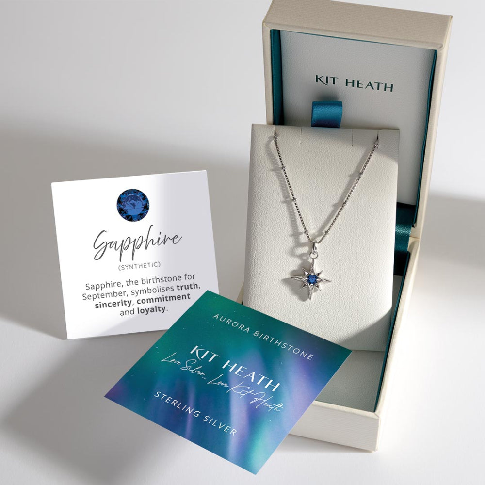 Silver necklace with star pendant and blue gemstone in a Kit Heath box, accompanied by information cards.
