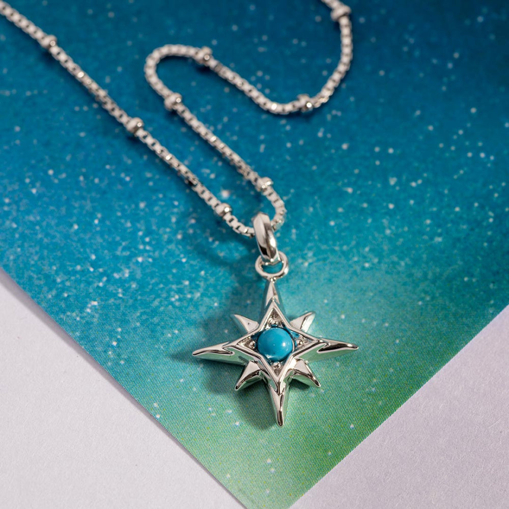 Silver necklace with a star-shaped pendant featuring a turquoise stone on a gradient blue and green background.