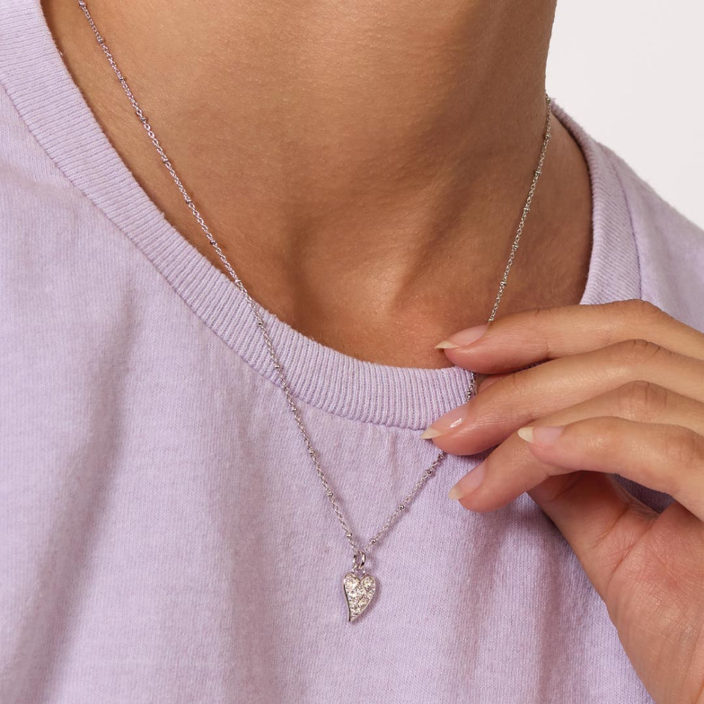 Necklace with a heart-shaped pendant worn by a person in a light purple shirt.