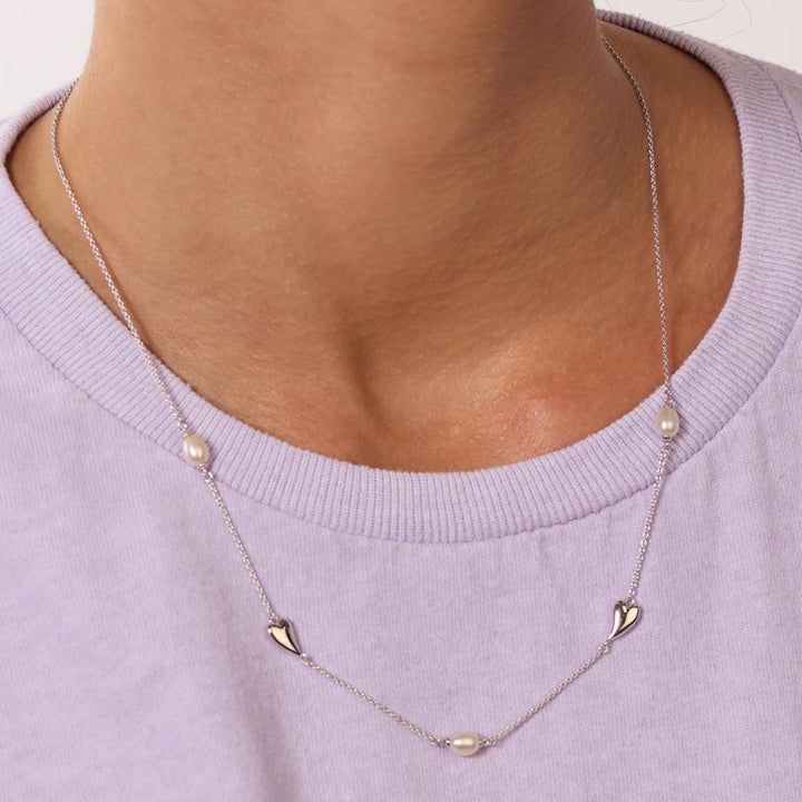 Necklace with heart and pearl pendants on a person wearing a light purple sweater.
