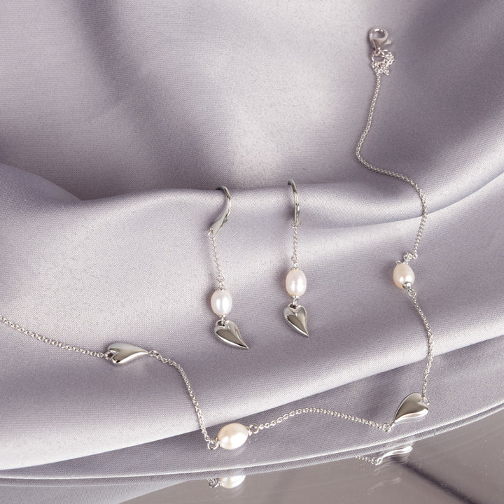 Silver jewelry set with pearls on a soft gray fabric background