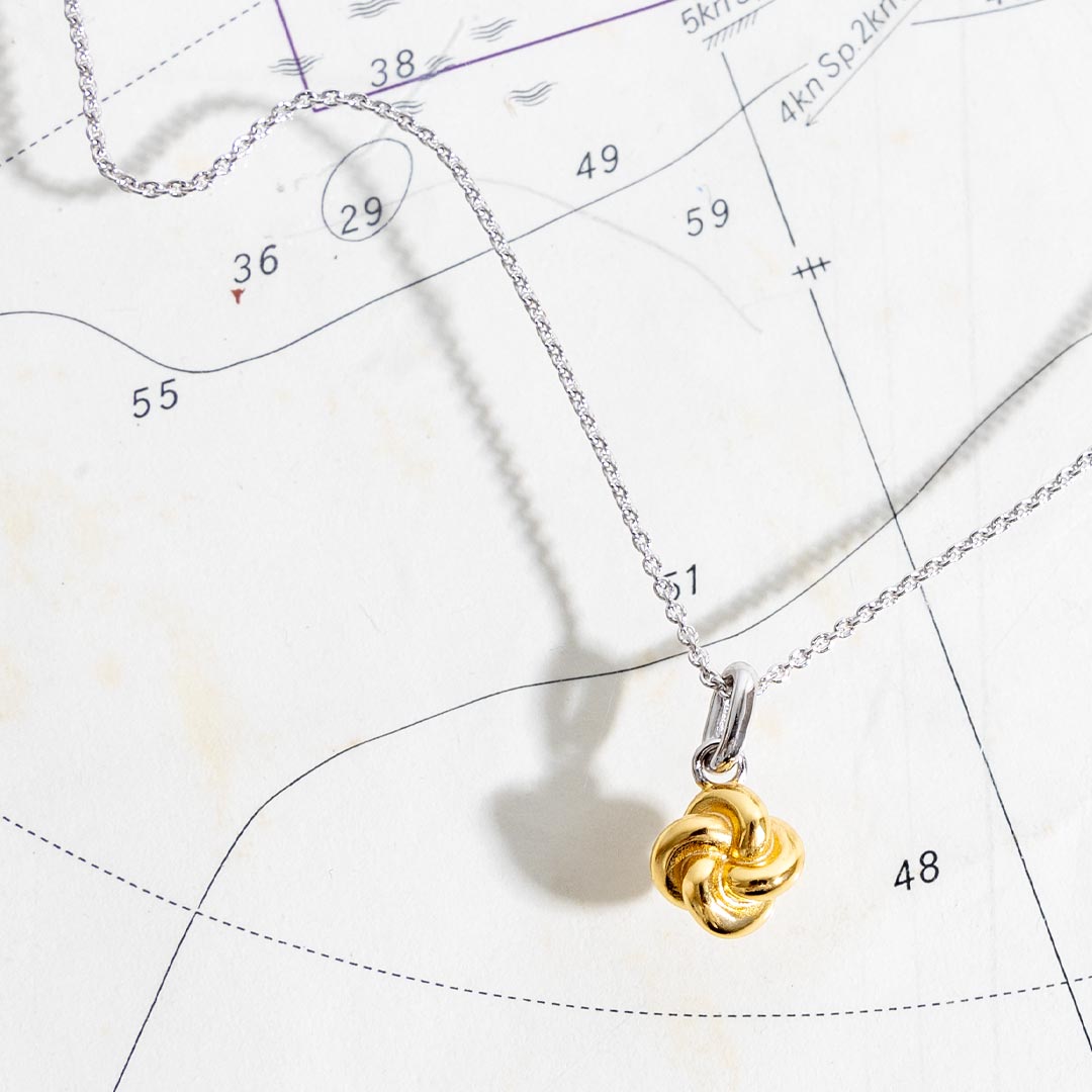 Gold knot pendant on a silver chain against a star map background